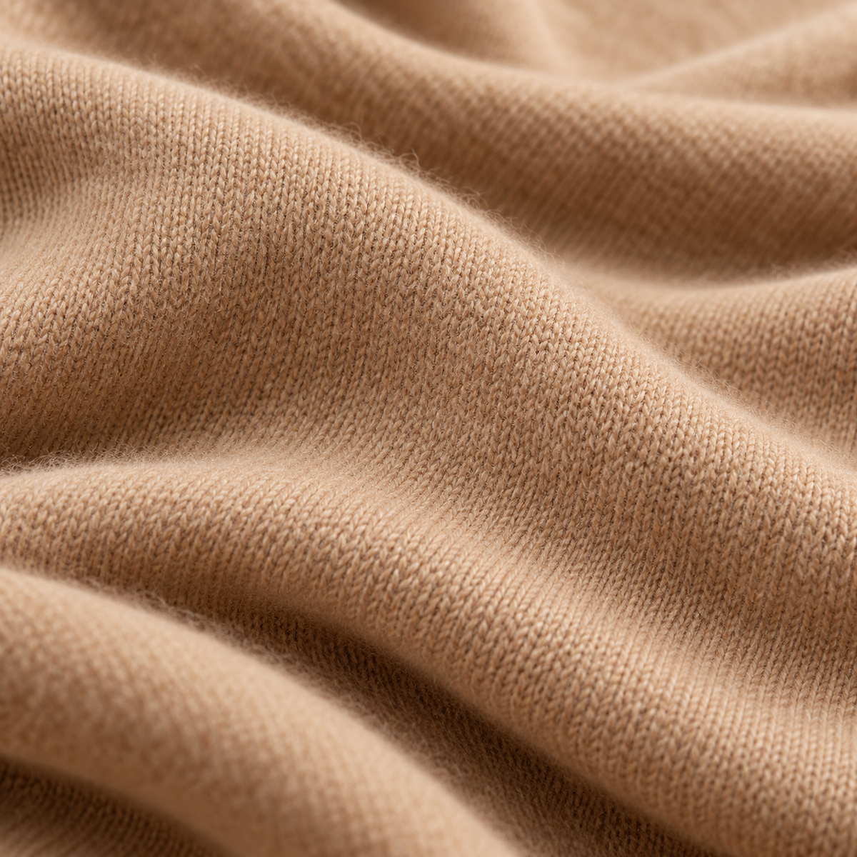 Close-up of camel cashmere knit with delicate fibers and soft, flowing folds.