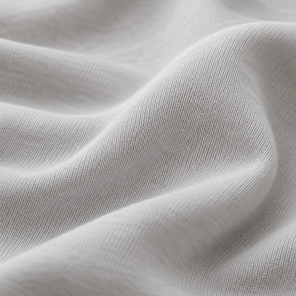 Close-up of light grey cotton jersey fabric with fine knit texture and soft, flowing folds.